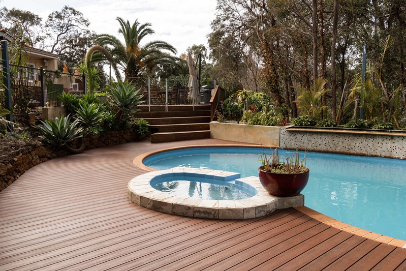 A backyard with a wooden deck and a swimming pool featuring composite decking.