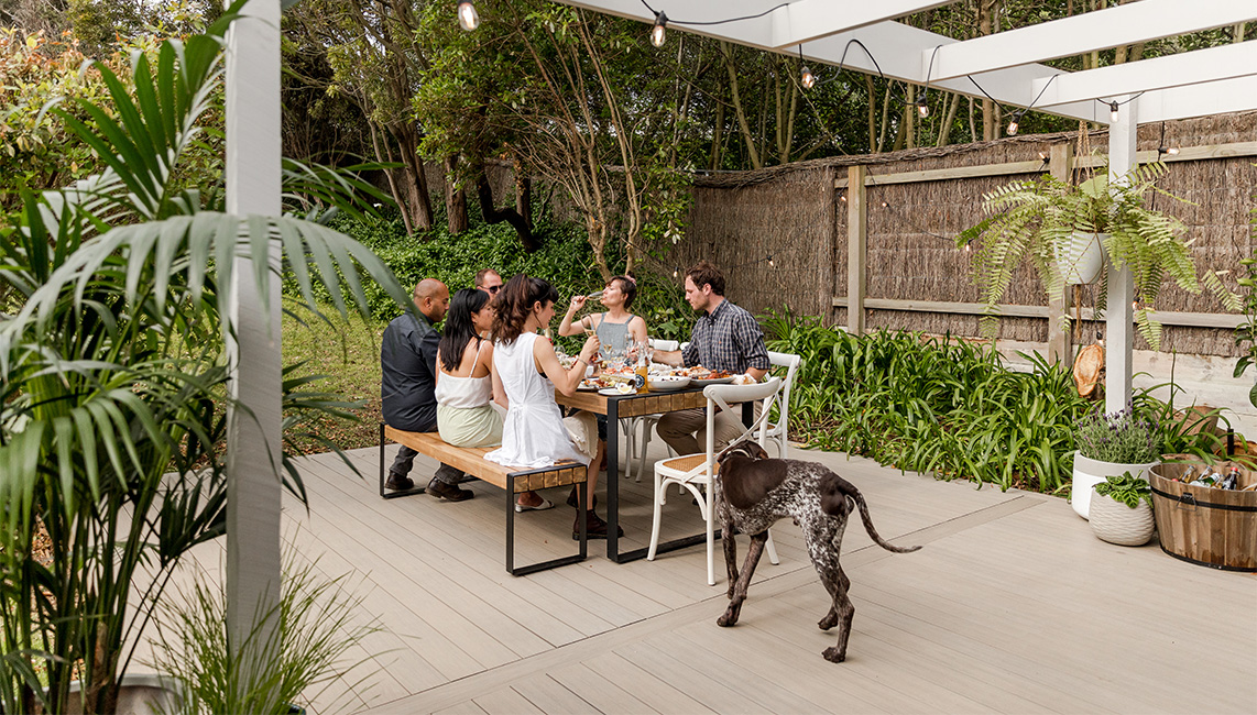 A group of people sitting around a table with a dog on composite decking.