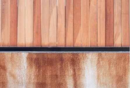 A wooden wall featuring rusty paint on it, alongside composite decking.